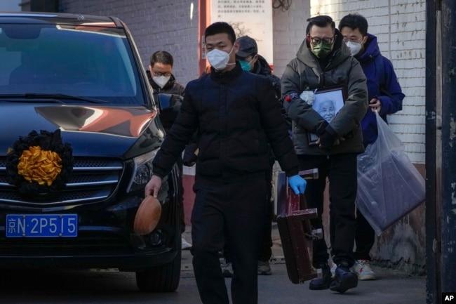 北京一个发热门诊外,一名亲属手拿去世亲人的照片走过一辆灵车。(2022年12月19日)
