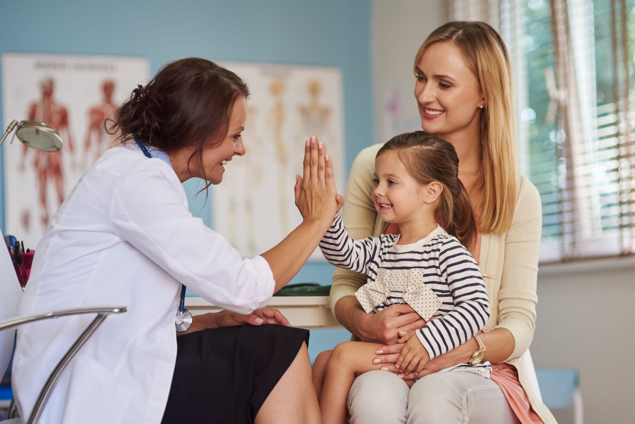 Na imagem, há uma garotinha acompanhada de sua mãe em consulta com uma médica