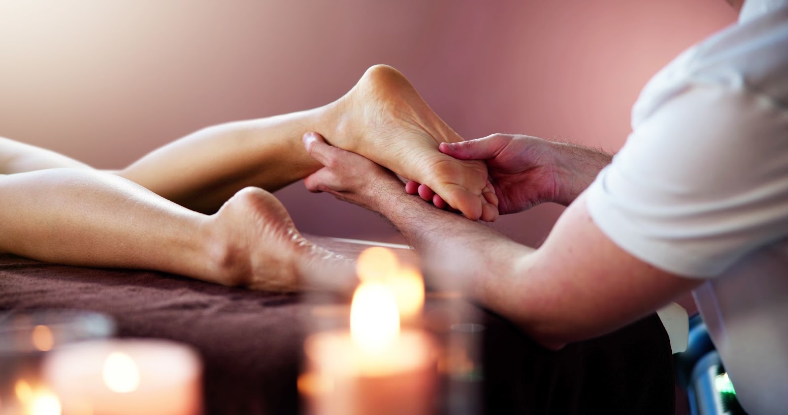 A person receiving foot reflexology treatment in a relaxing room lit with candles.