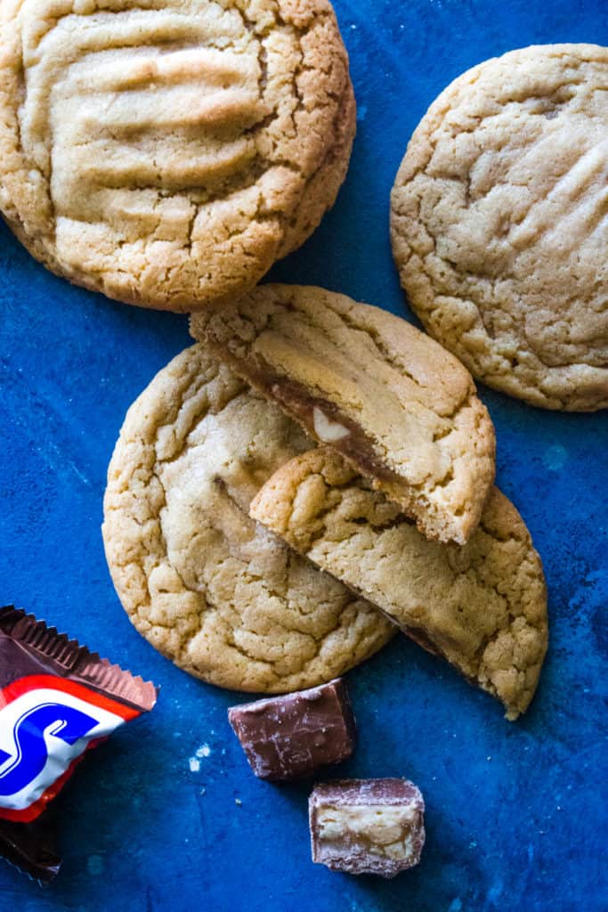 Cookies laying out on blue background with one cut in half and mini snickers. 