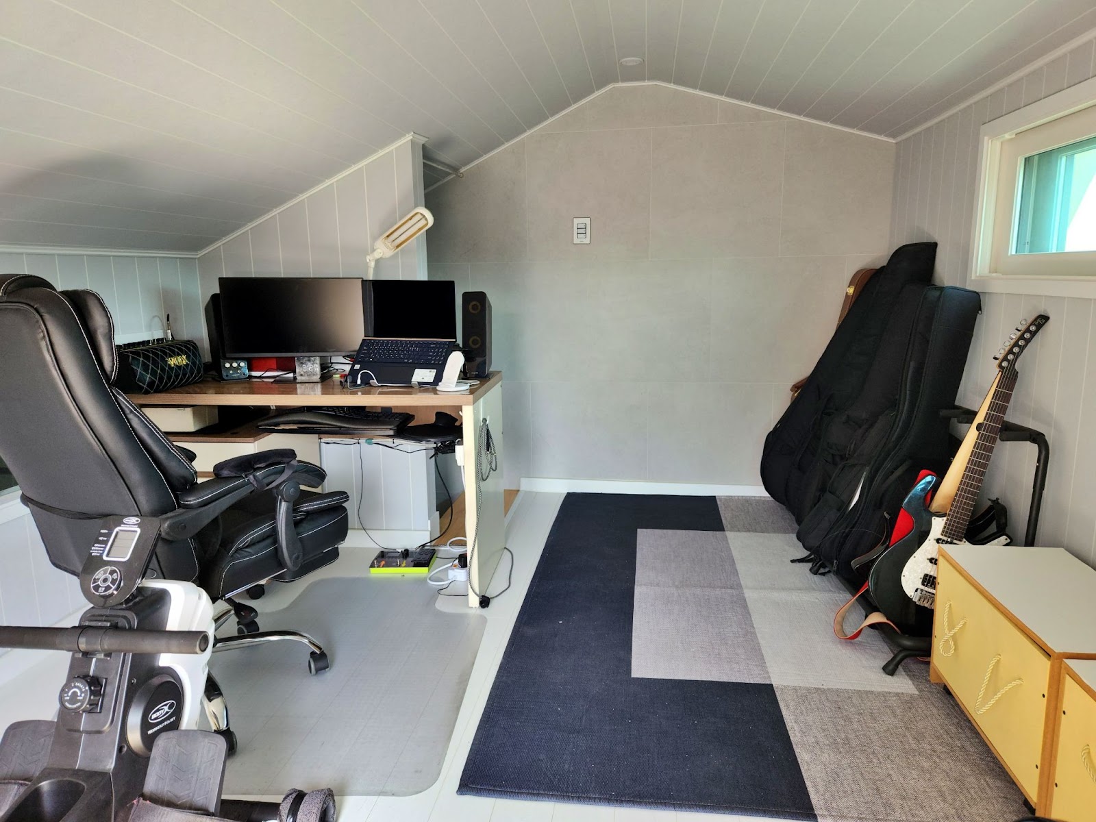 My loft office with several guitars on the right and a desk with a laptop and a second monitor on the left.