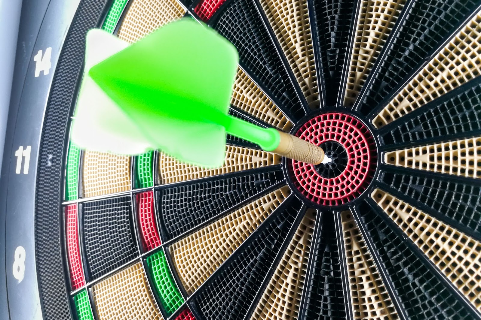 Green dart hitting a dart board's center for a bullseye 