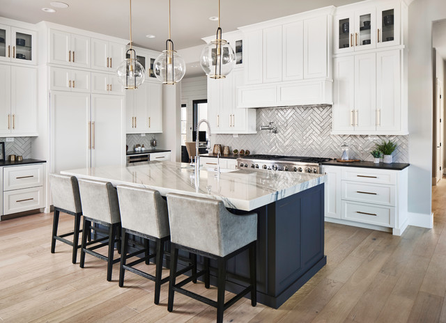 white shaker kitchen with paneled appliances, large center island, brass cabinet hardware, wood floors and glossy herringbone tile backsplash