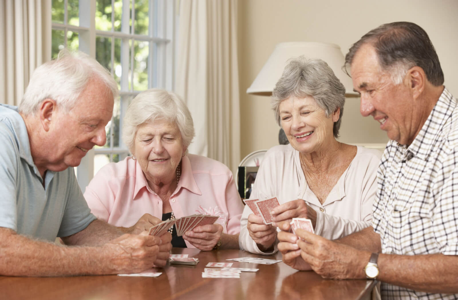 A group of 4 seniors are sitting at the table while enjoying playing cards.