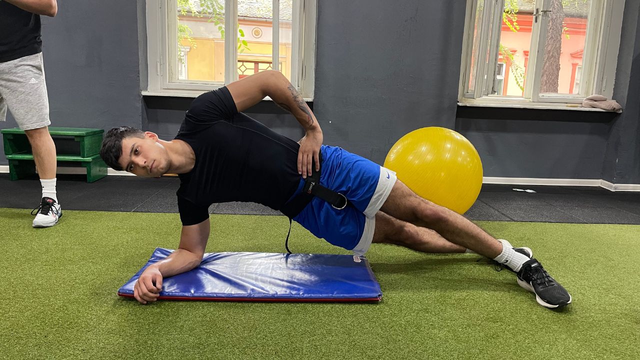 Vanja performs the side plank exercise for the lower back in the commercial gym setup.