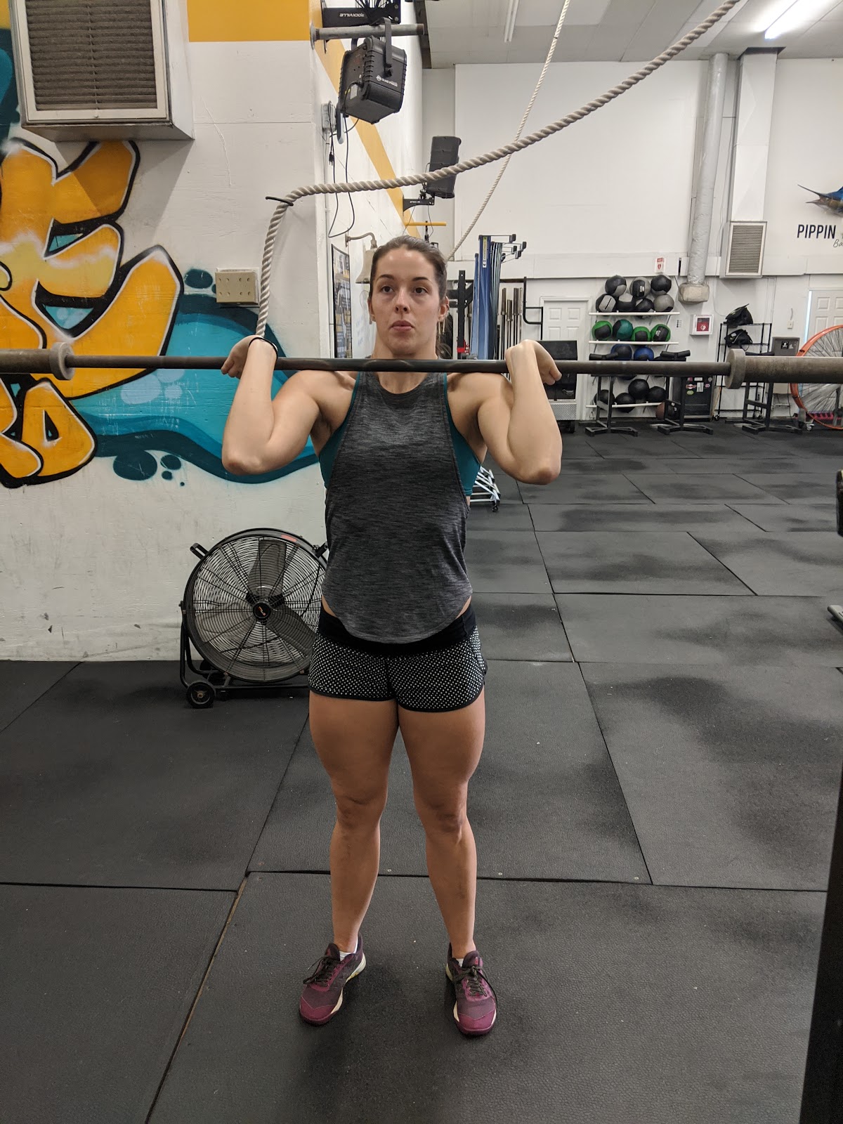 front view of woman in drive for split jerk with empty barbell on shoulders
