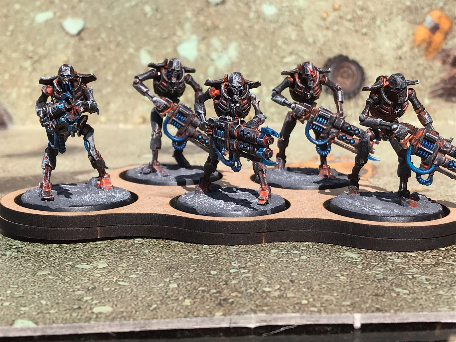 A unit of five Necrons, skeletal robot warriors. They are painted in dark coal colours, with orange light glowing from inside.
