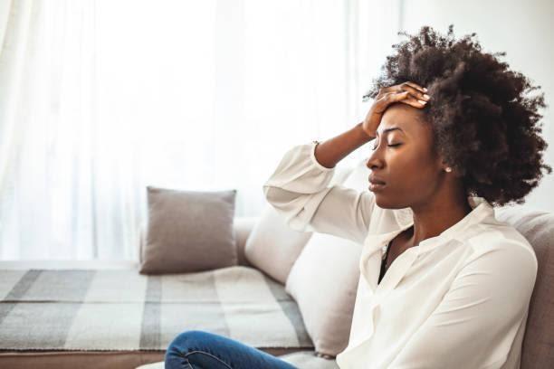Shot of a young woman suffering from a headache. Lonely sad woman deep in thoughts sitting daydreaming or waiting for someone in the living room with a serious expression, she is pensive and suffering from insomnia sitting on couch feeling relaxed stock pictures, royalty-free photos & images