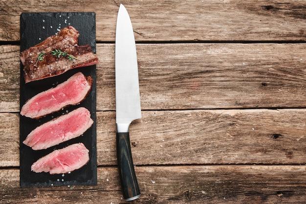 Premium Photo | Slices of superior grilled meat served on black slade  placed on rustic wooden table with copyspace for text.
