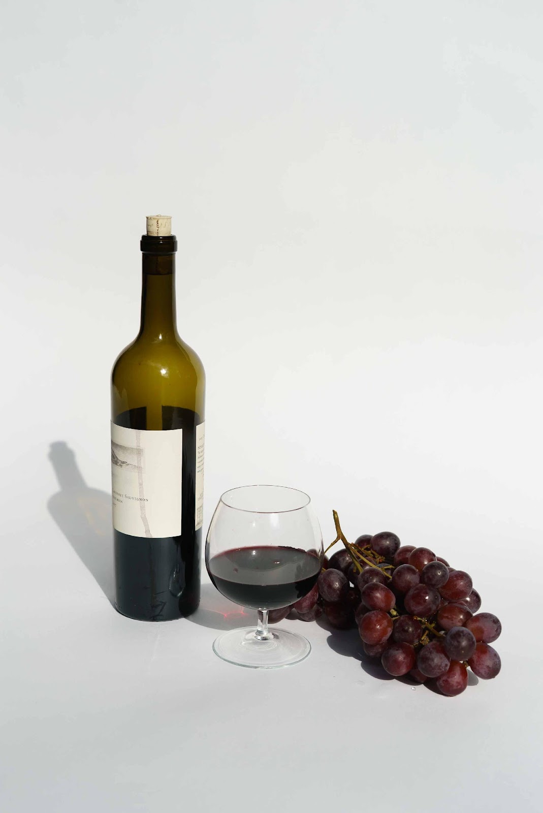 A bottle of wine, a glass with half-filled wine and a bunch of grape.
