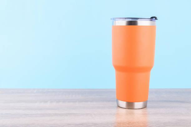 Orange steel  or stainless  thermos mug or cup For keeping heat or cold water put on wooden table isolated on bule pastel background. Orange steel  or stainless  thermos mug or cup For keeping heat or cold water put on wooden table isolated on bule pastel background. insulated tumbler stock pictures, royalty-free photos & images