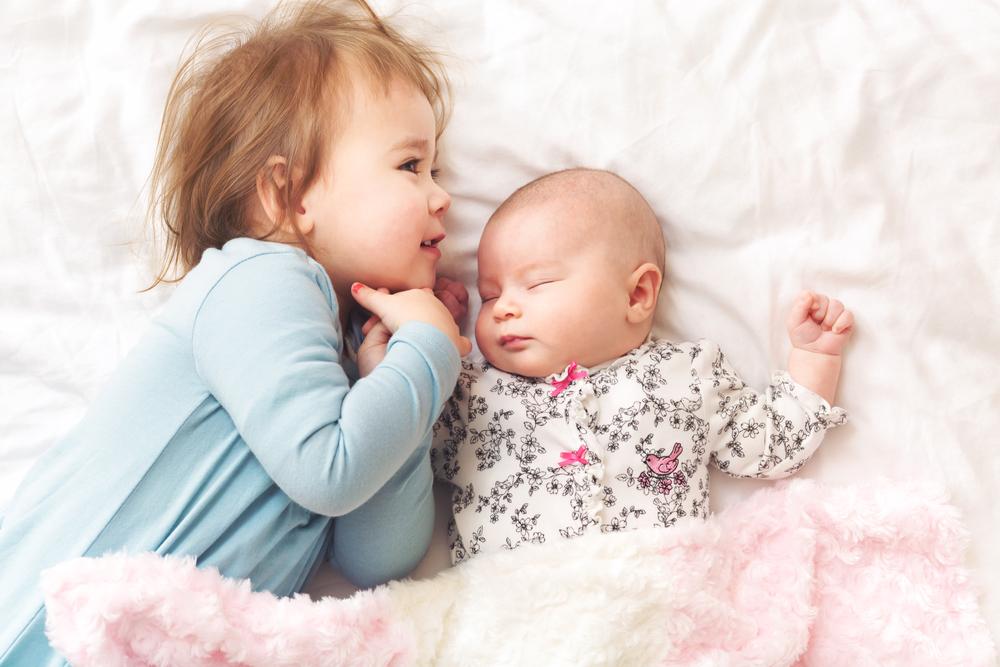 Happy toddler girl playing with her newborn sister