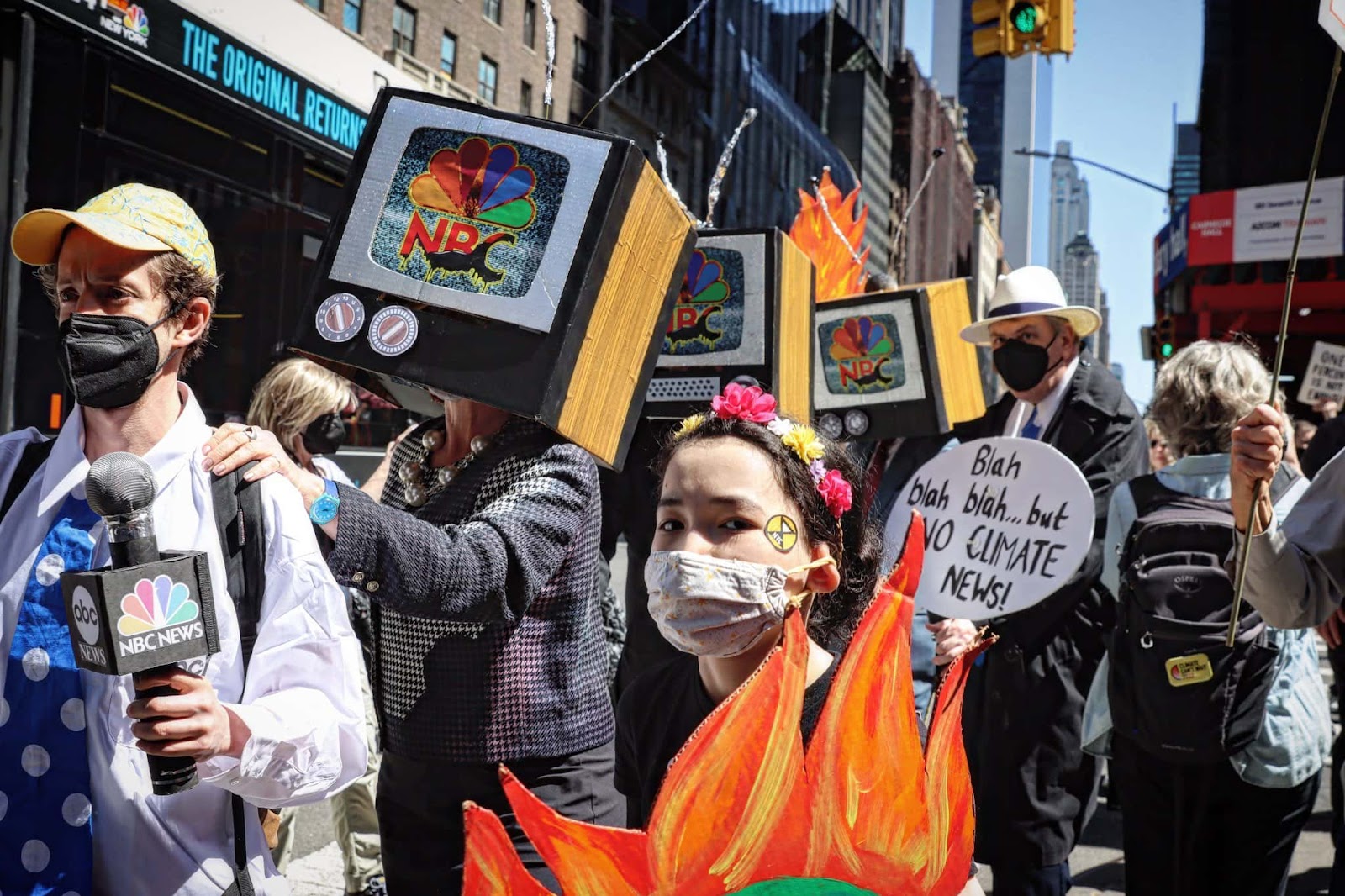 Rebels with tv set helmets and fire ensignia march outside the NBC offices in New York