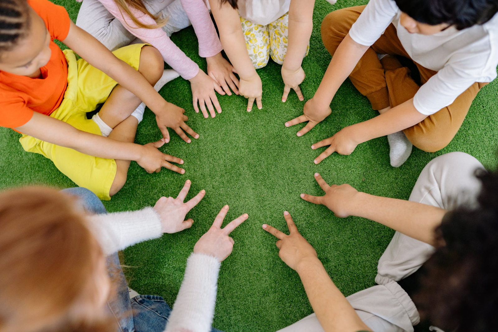 children sitting in a circle making peace or two signs with their hands