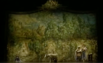 A stage with what looks like a tapestry hanging on it. Indiscernible figures stand in front of it.