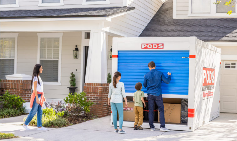 A family of four closes the door on their PODS container after loading it in their driveway.