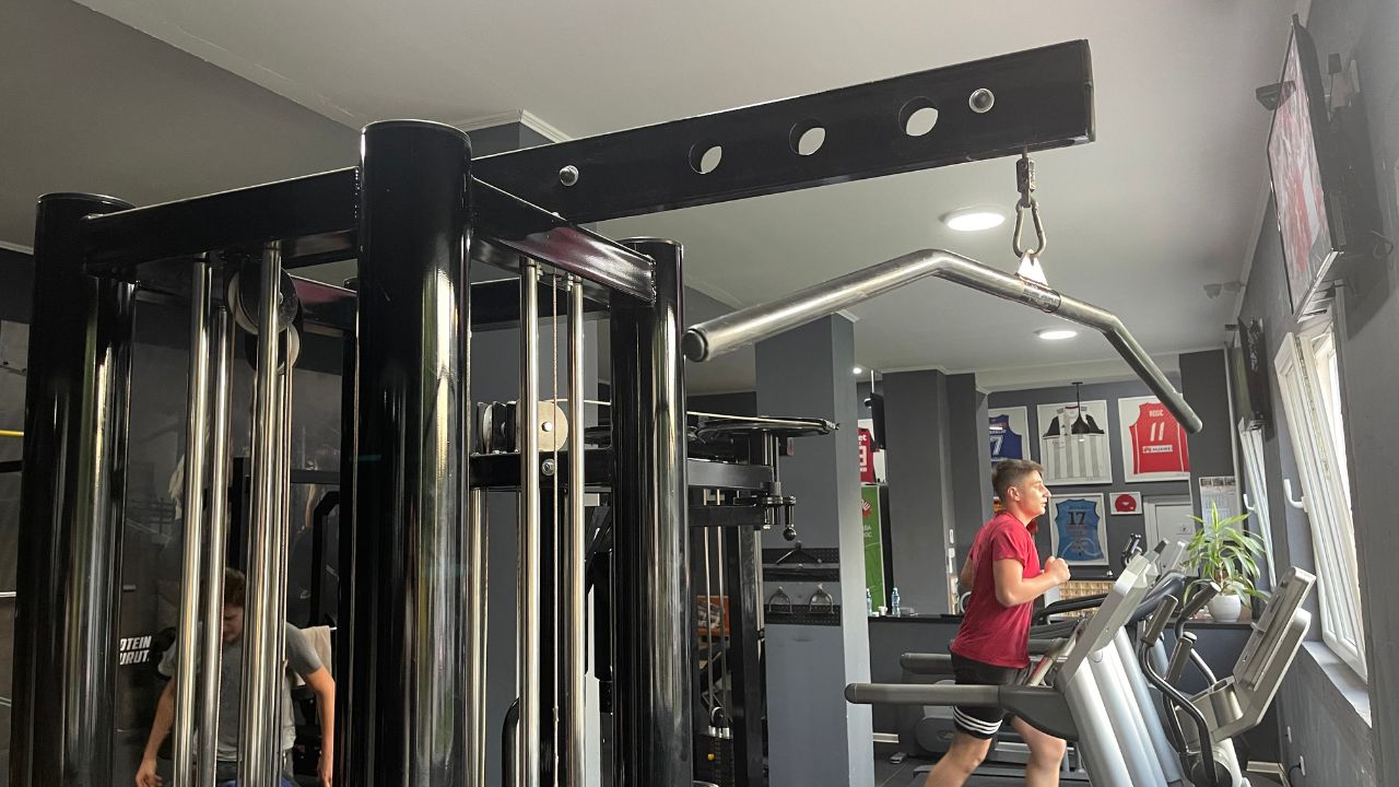 The image showcases a lat pulldown machine in a commercial gym setup.