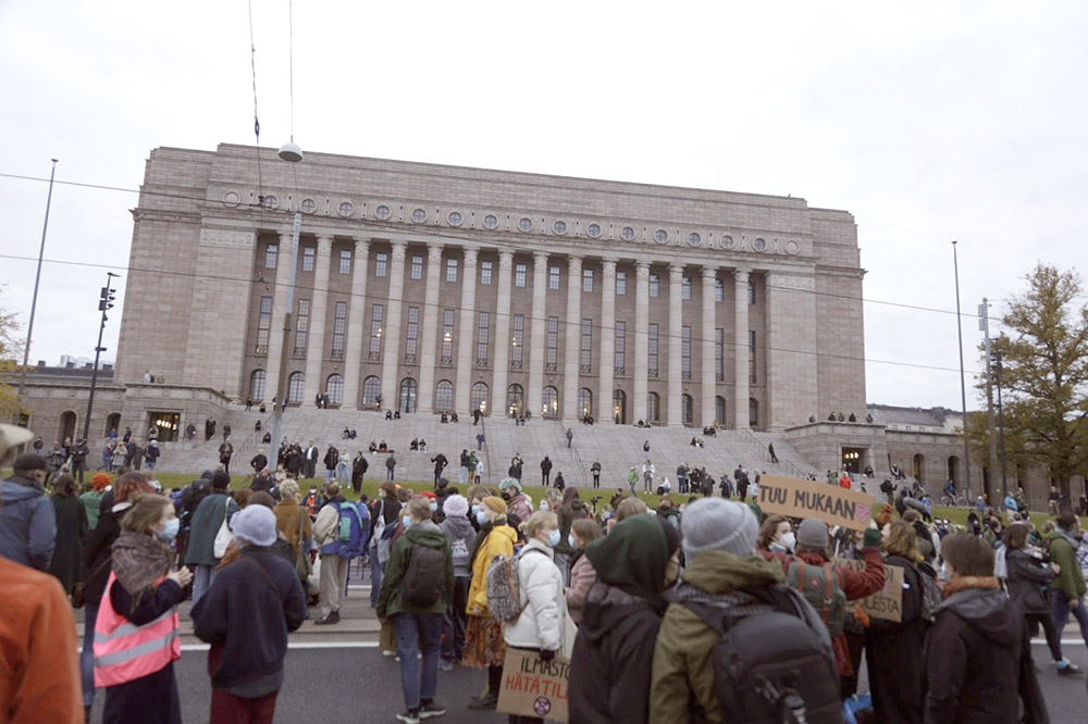 Rebels mingle in clusters, signs held low, outside the Finnish parliament.