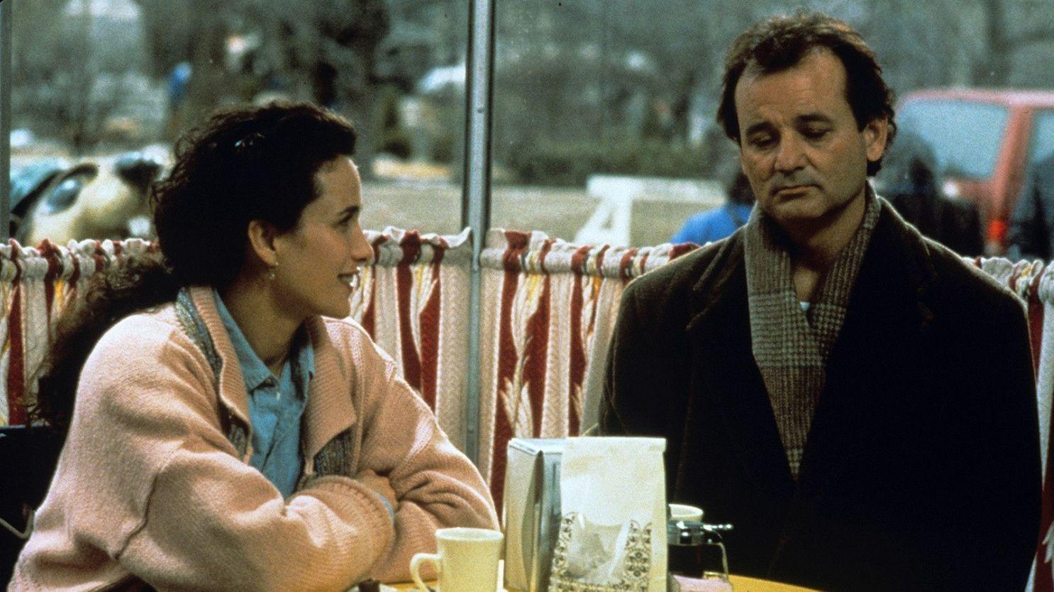 This is a screen still from Groundhog Day. A man and a woman sit at a table in. a breakfast restaurant. The man looks down and upset.