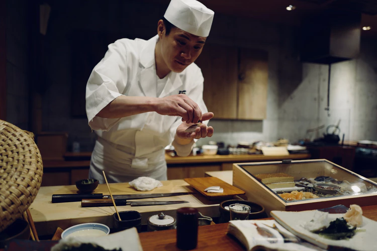 Japanese chef seasoning and cutting food on wood cutting board