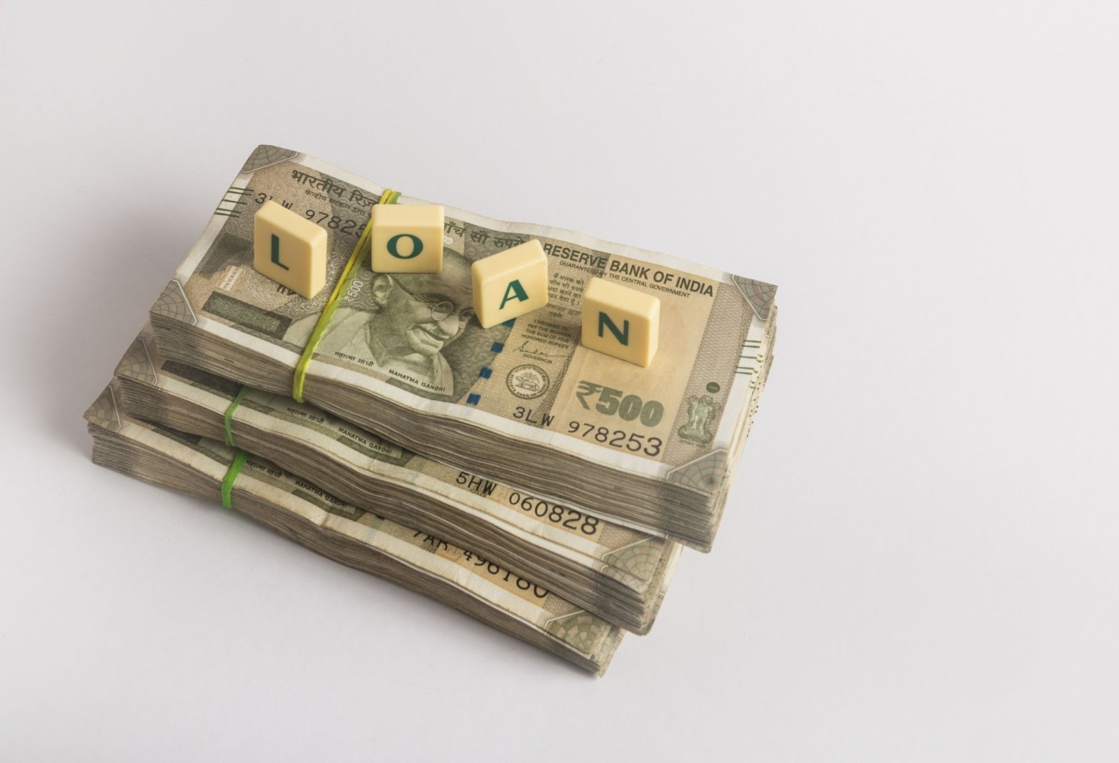 A picture of stacks of money from the Reserve Bank of India, that has letters on tiny plastic block that spell out LOAN.