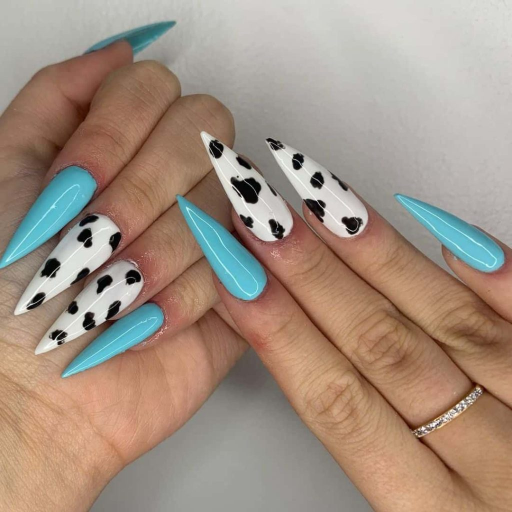 Close up photo of a lady rocking a  mix match blue and cow print nail design