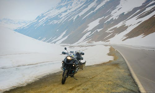 A motorbike parked by a roadside in winter. The bike's headlight is on since wintry conditions often lead to poor visibility on the roads.