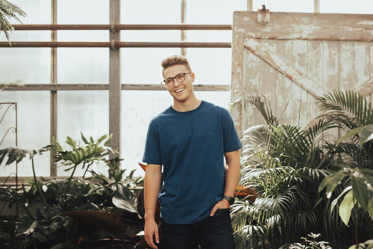 Un'uomo con degli occhiali da vista che indossa una t-shirt in un ufficio con alcune piante