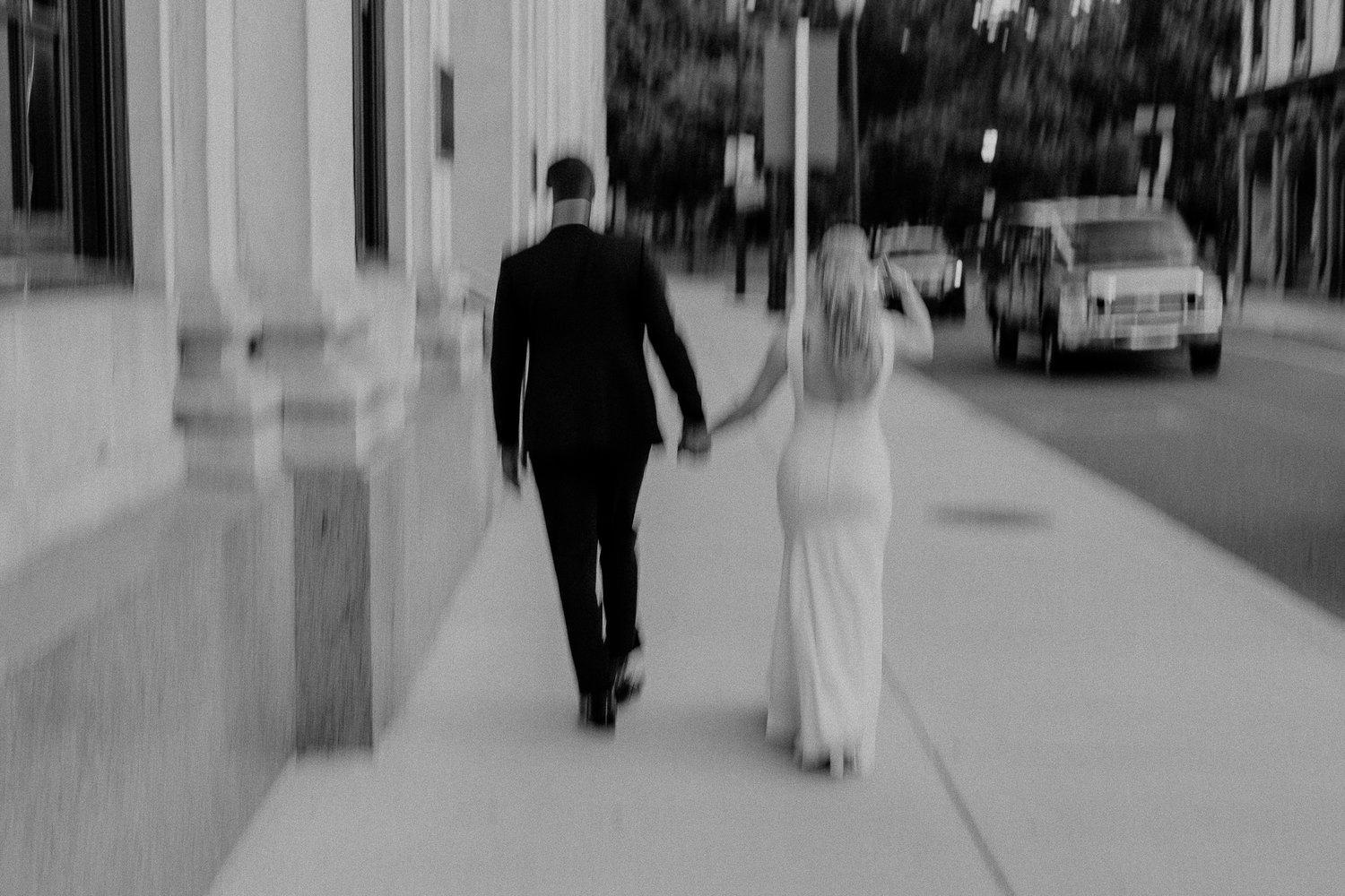 Intentionally blurry photo of a newly married couple holding hands while they walk down the street