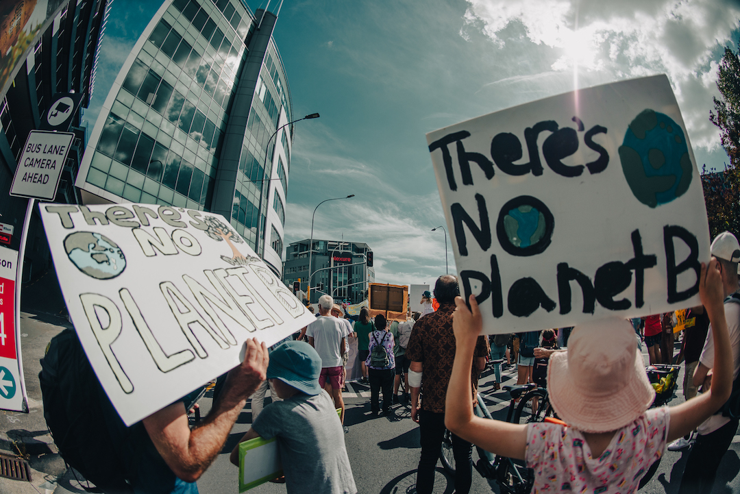A fishbowl photo of a street scene with two placards in the foreground both saying: There's no Planet B