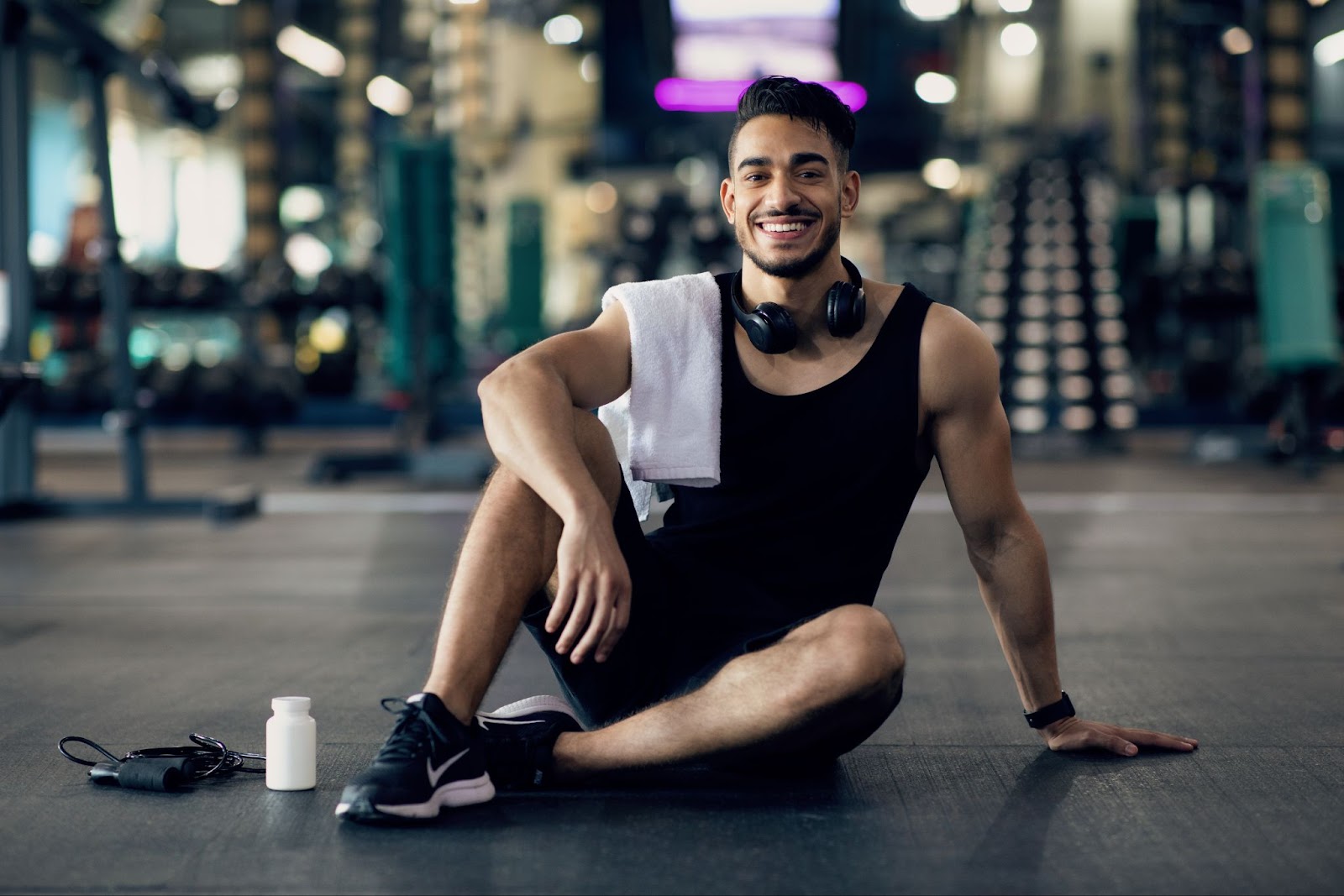 A young man sitting down in a gym smiling. 