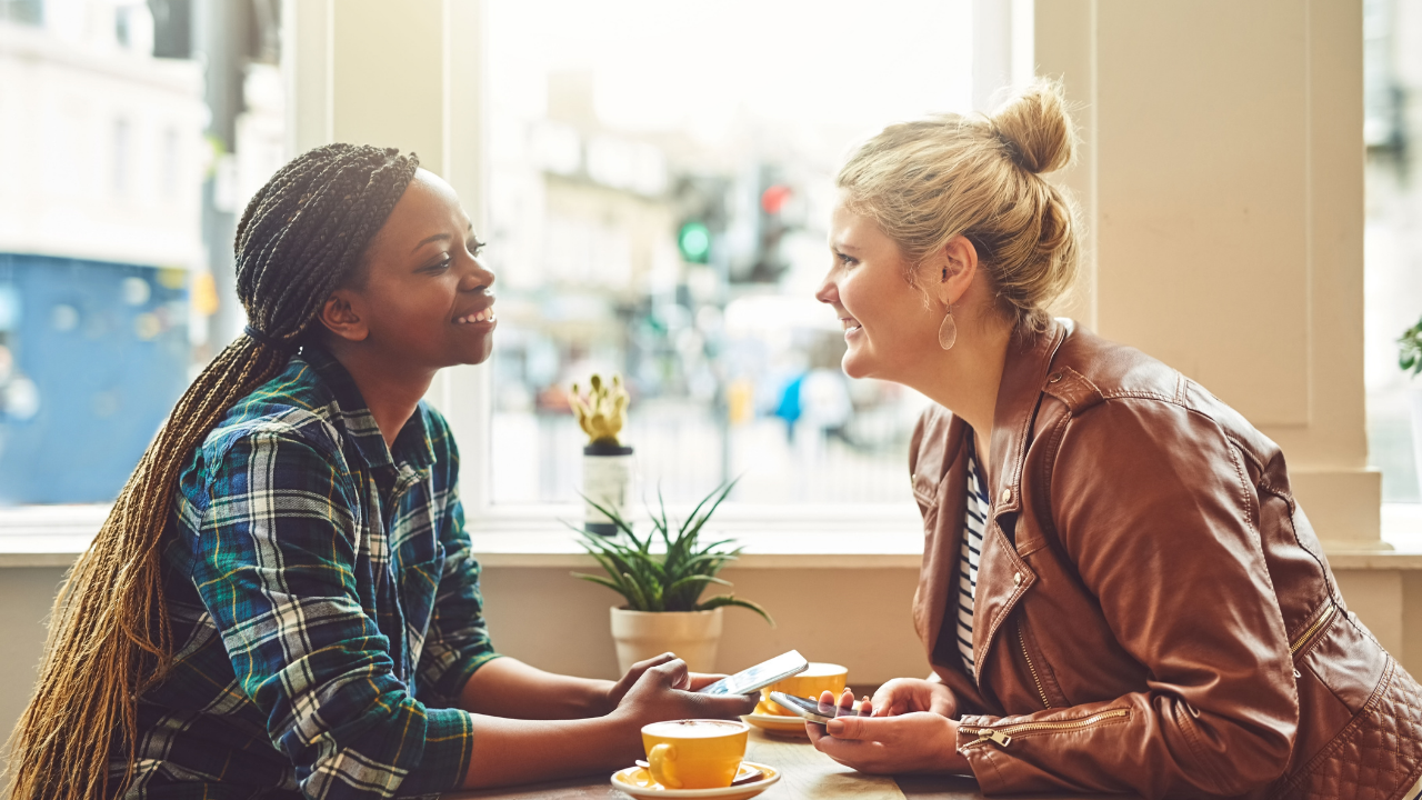 Two women talking to each other in a coffee shop, profiles smiling at each other