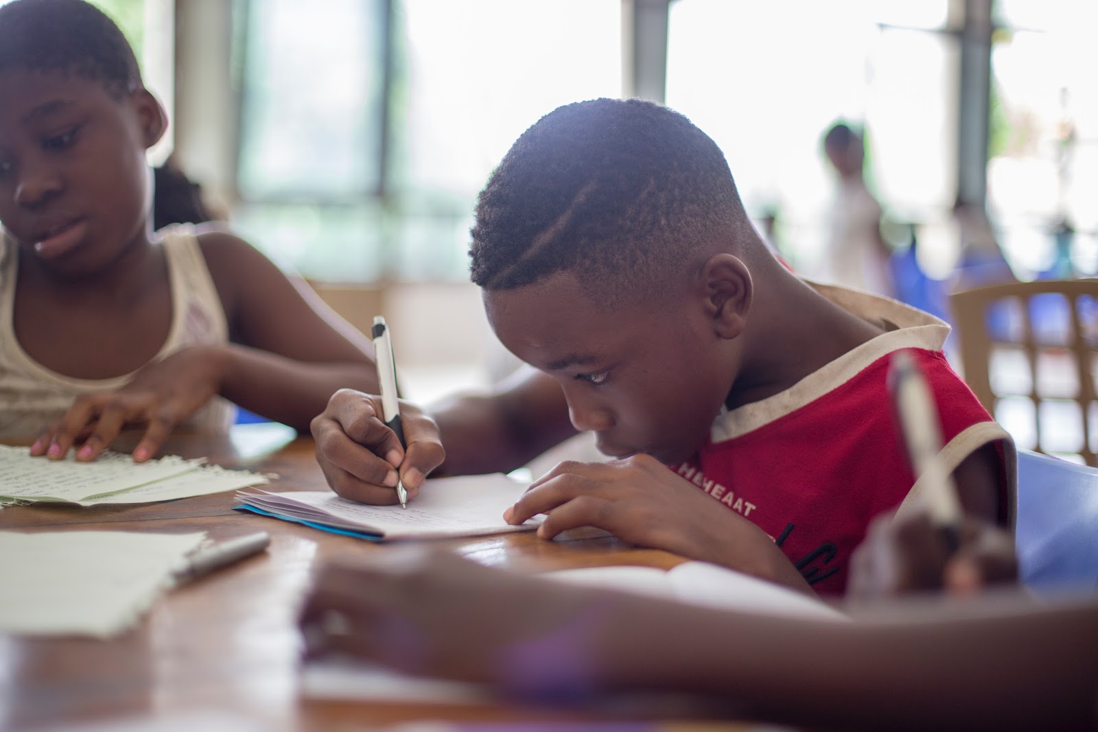 Two elementary age children - a boy and a girl - work at a desk writing observations and notes on paper.