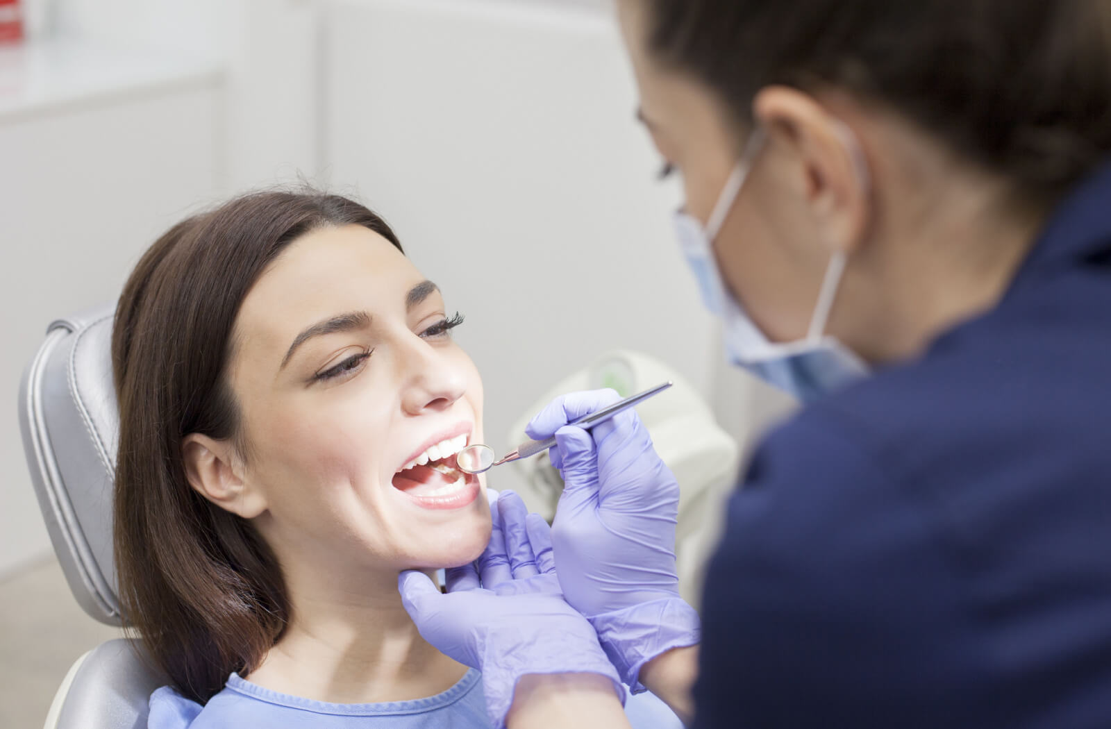 A woman sitting in a dentist's chair while a female dentist examines her teeth.