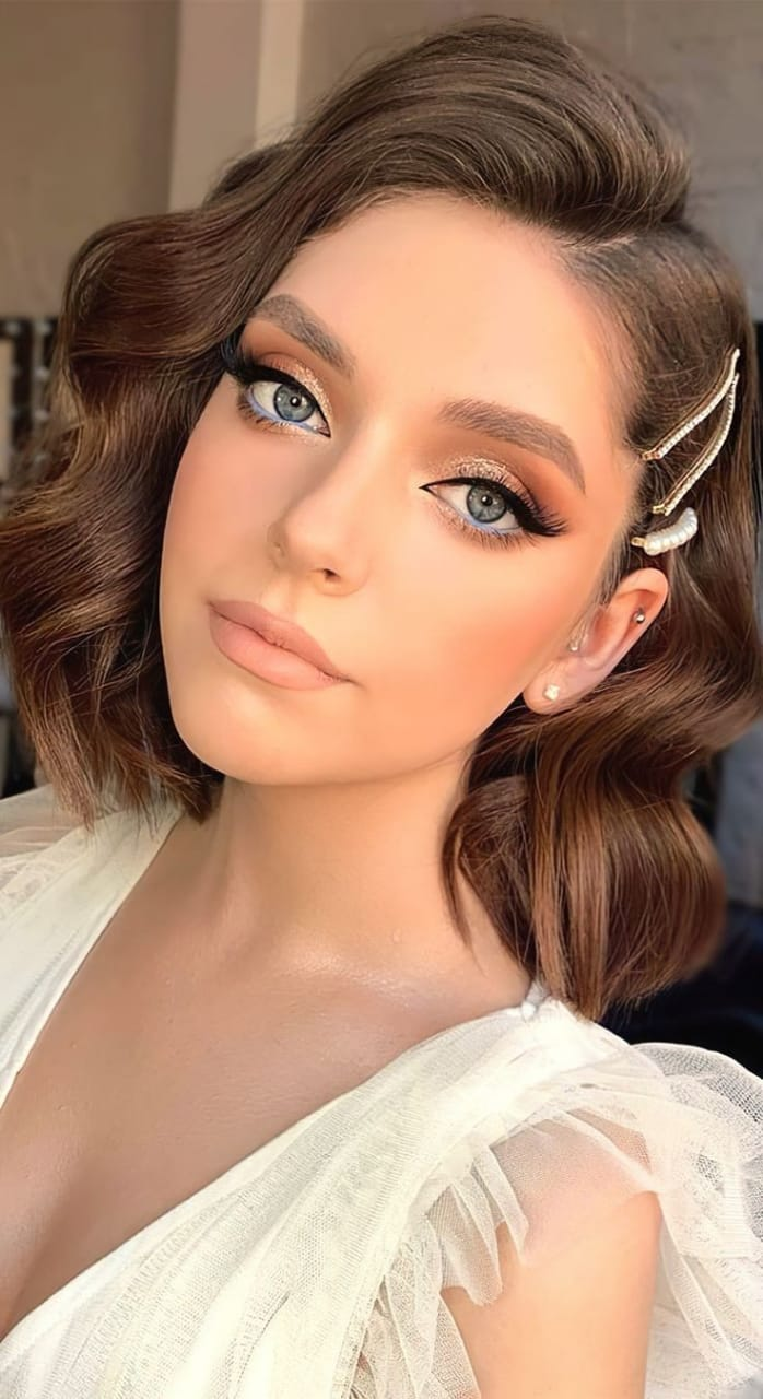 A lady wearing waves on short hair and adorning it with a gold barrette