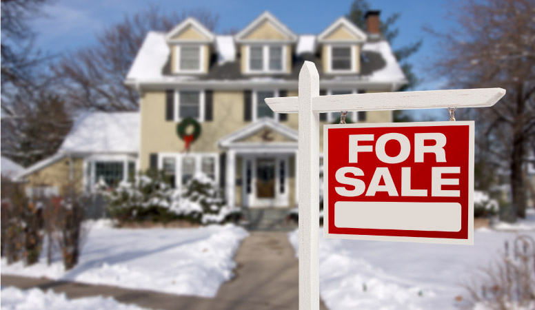 A "For Sale" sign in front of a snow-covered home