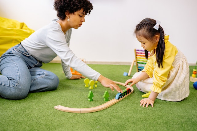 woman playing with train toy with young girl