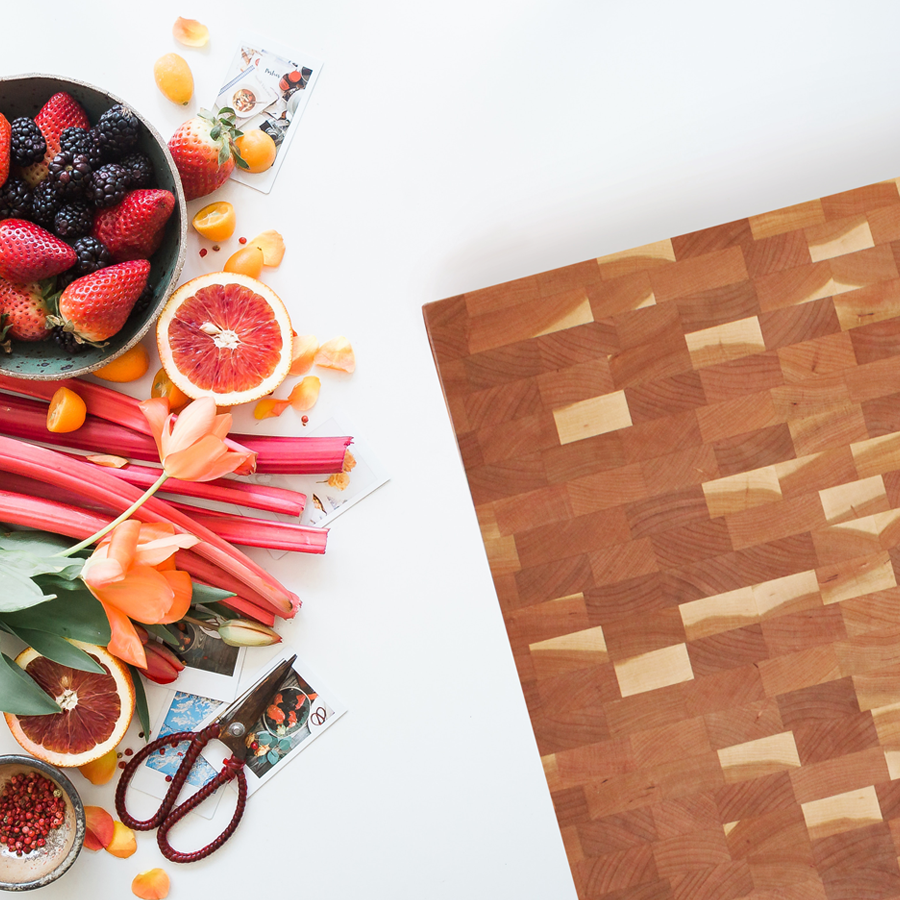 Wooden cutting board with fruit and flowers nearby