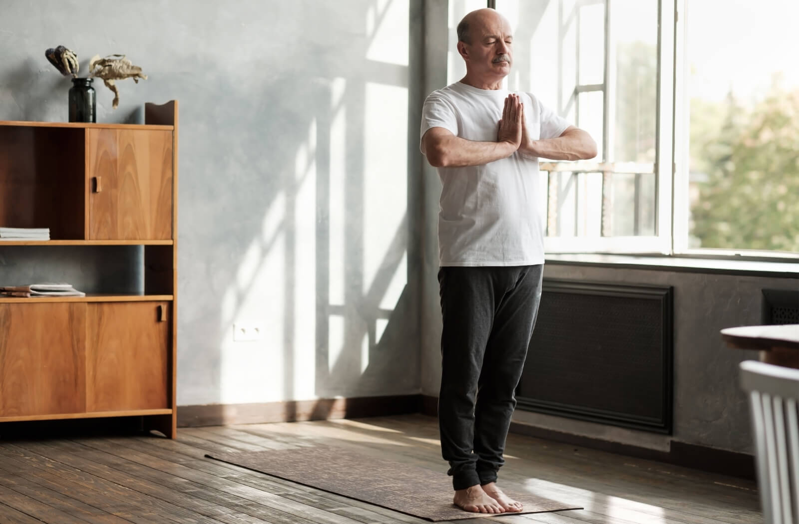 A senior man in his active wear doing yoga in a brightly lit room.