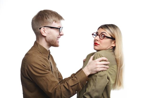 Furious young bearded male in eyewear shaking his frightened wife by her shoulders. scared woman in glasses being abused by her angry husband. people, marriage, abuse and home violence concept Free Photo
