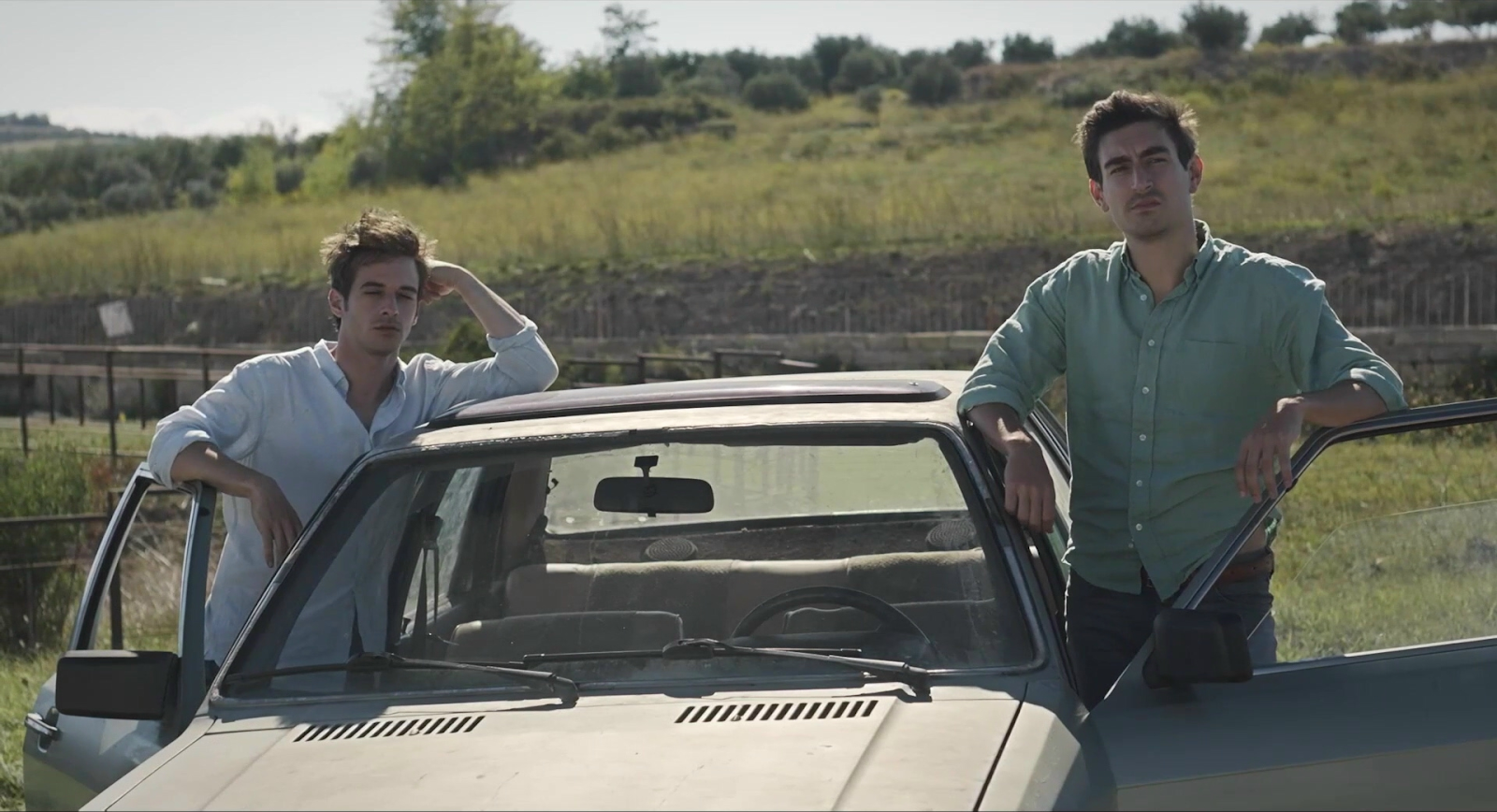 A still from The Man with the Answers, Vasilis Magouliotis as Victoras and Anton Weil as Mathias standing outside a car together. 