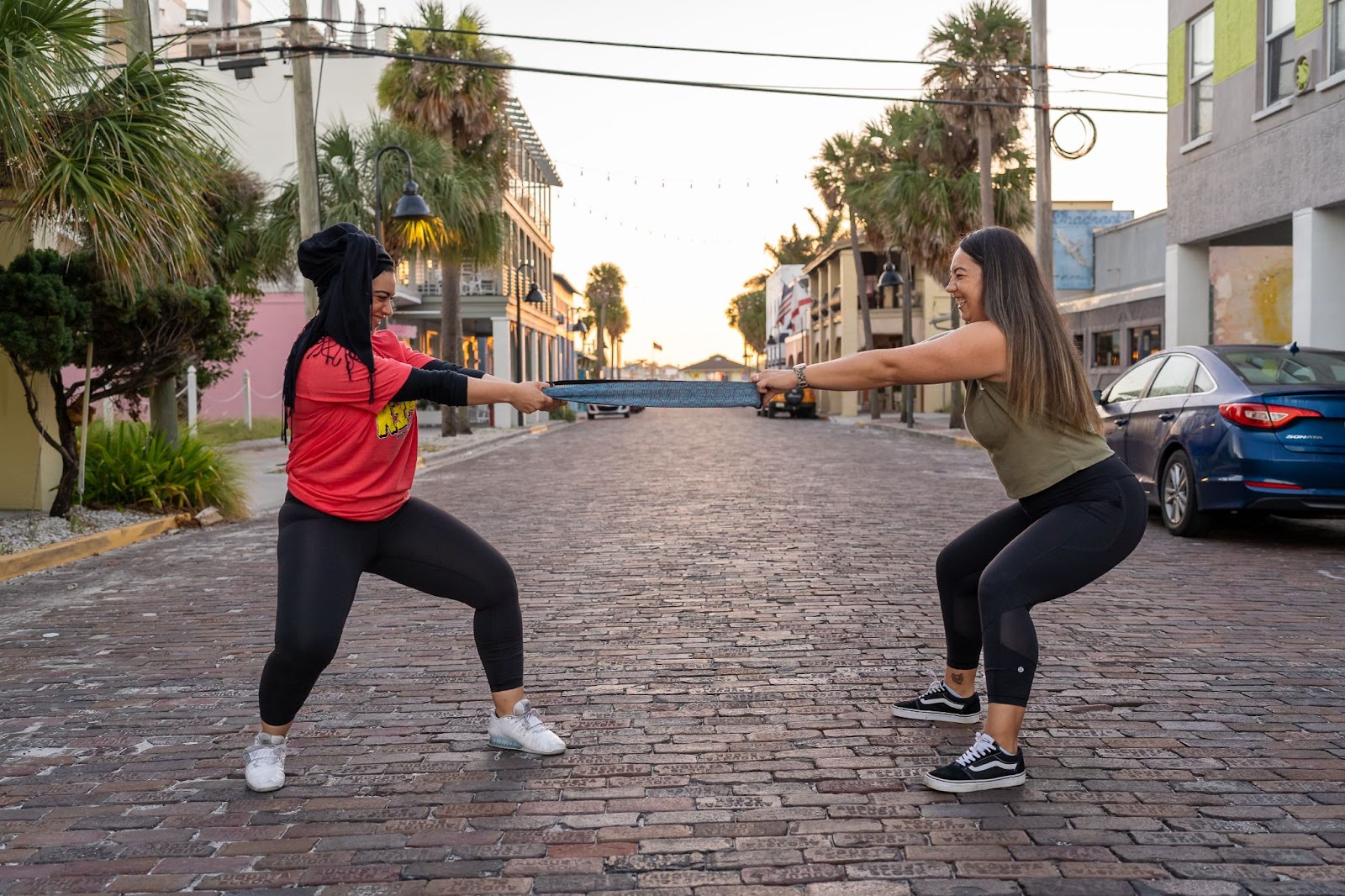 two female athletes smiling and playing tug with a glute band in the middle of the road