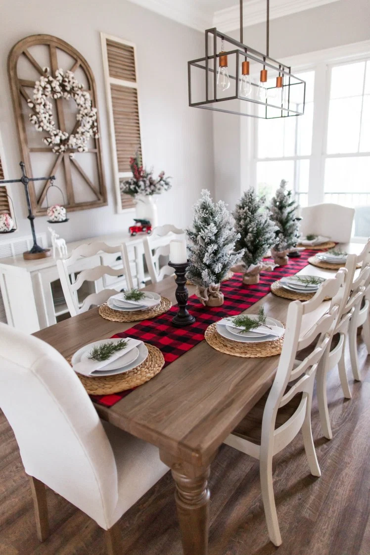 christmas kitchen table decor featuring buffalo plaid table runner, mini christmas trees, elegant modern place settings and a black pillar candle