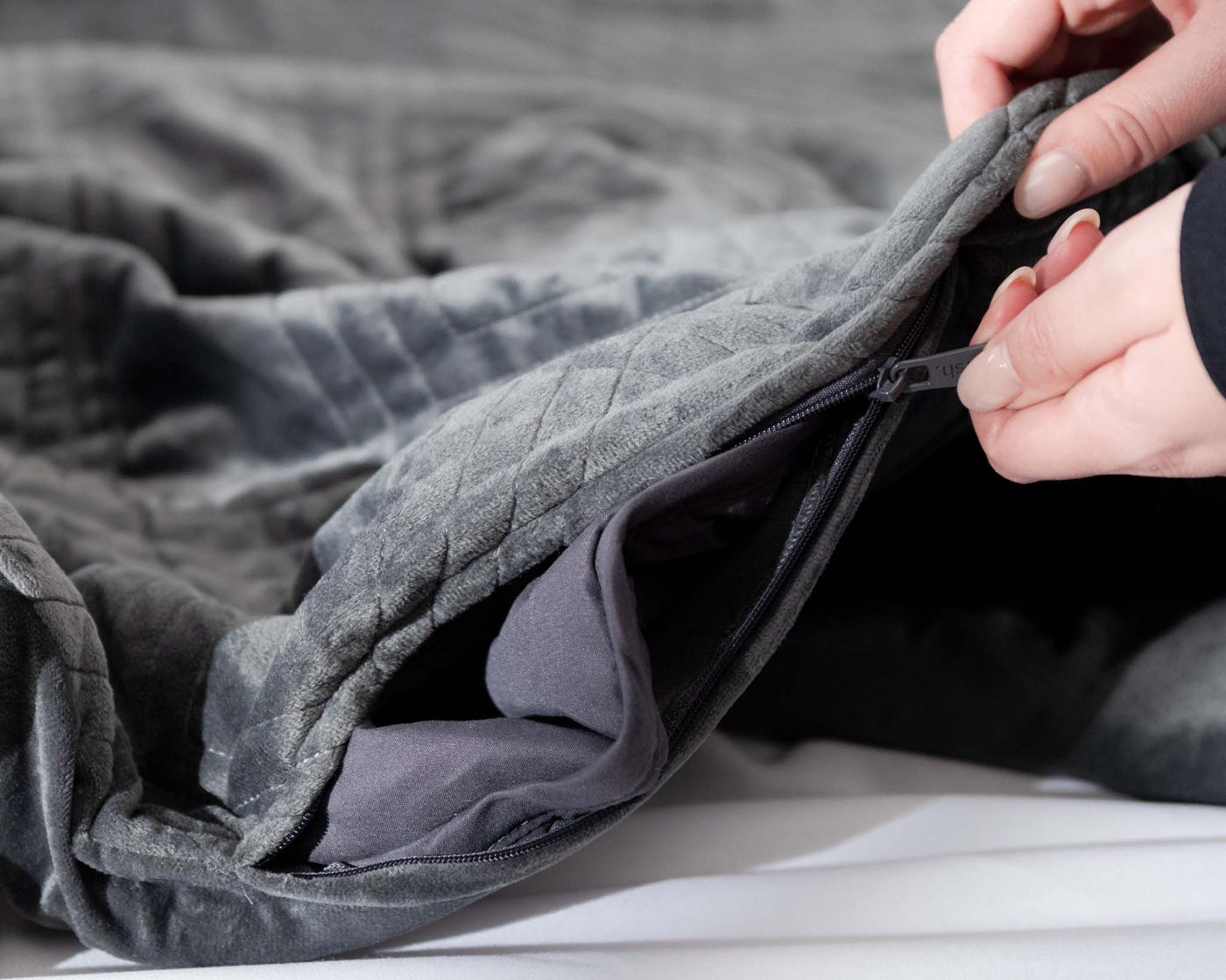 A person zipping up a Hush weighted blanket in classic gray color.