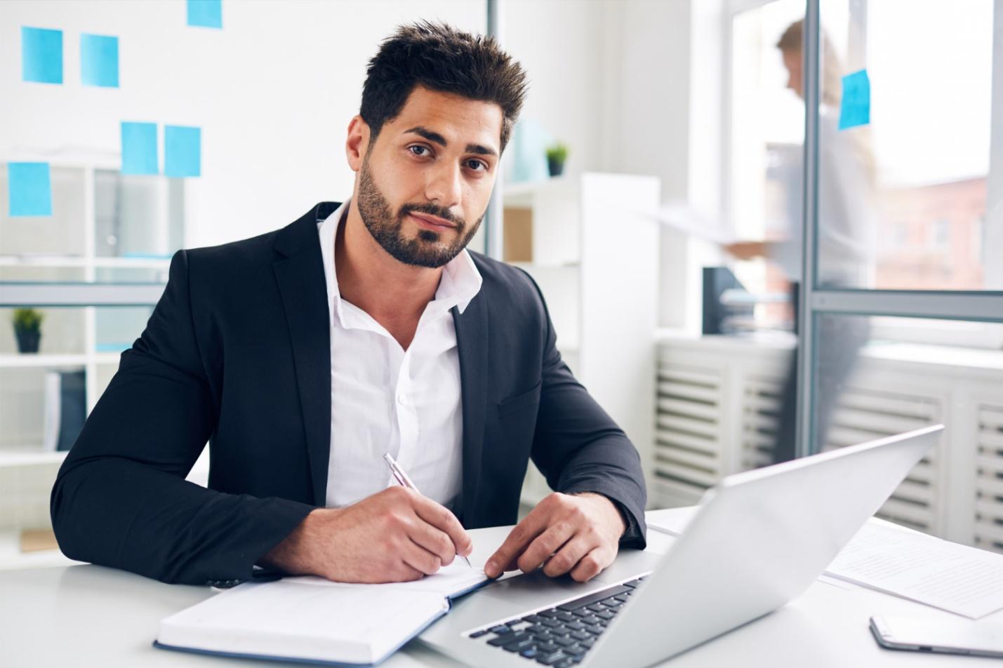 Strata Manager at work at a desk writing in note book next to laptop computer