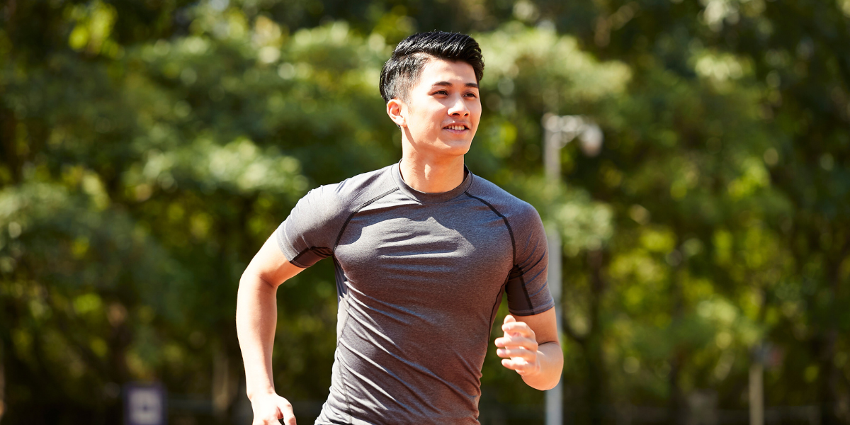 Gray-shirted man running on a track, displaying a happy and injury-free expression.