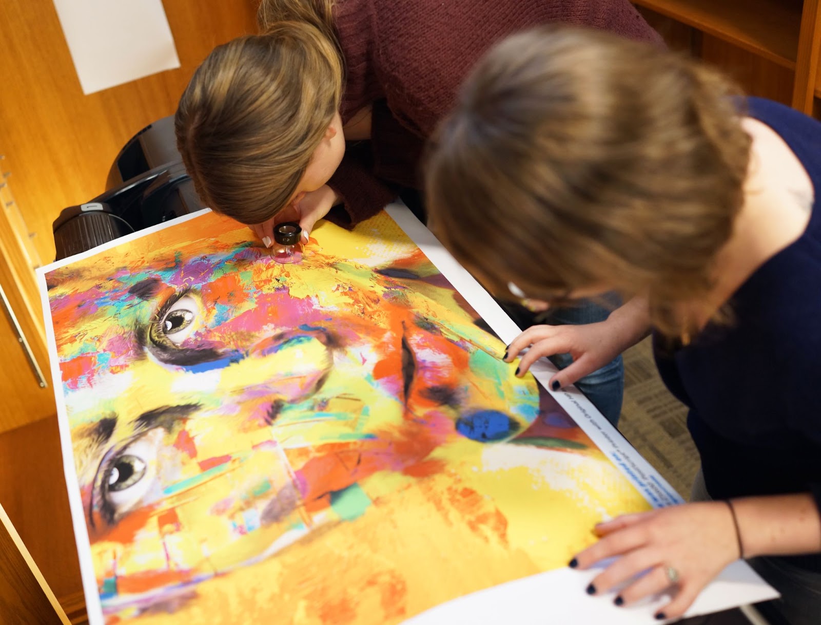 two people looking closely at a painting of a face