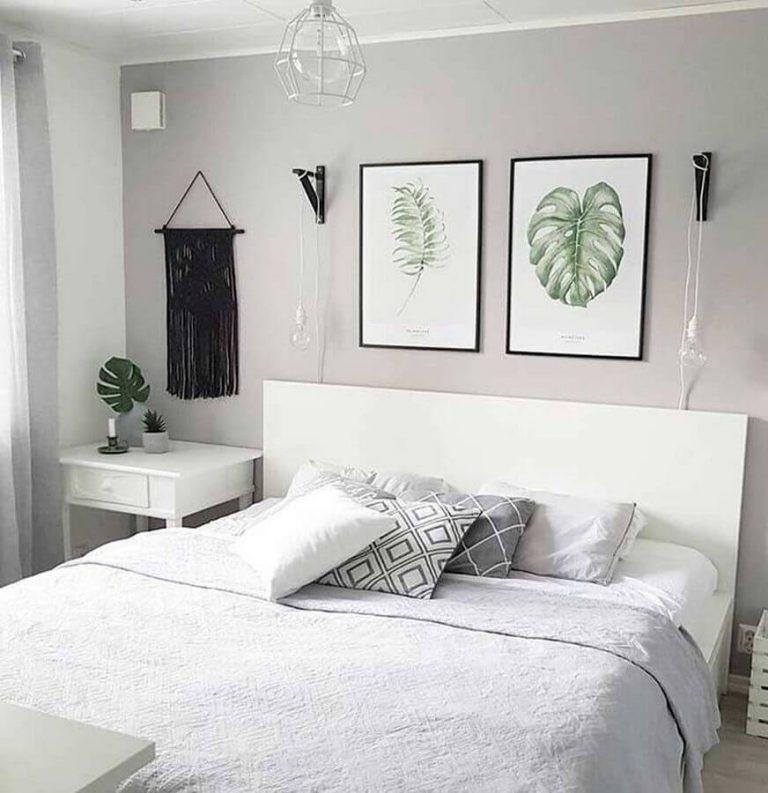 Quarto com decoração clean, cabeceira da cama de madeira e móveis brancos, parede de fundo cinza claro, quadros com imagens de planta e moldura preta, macramê preto  e luminárias pendentes brancas