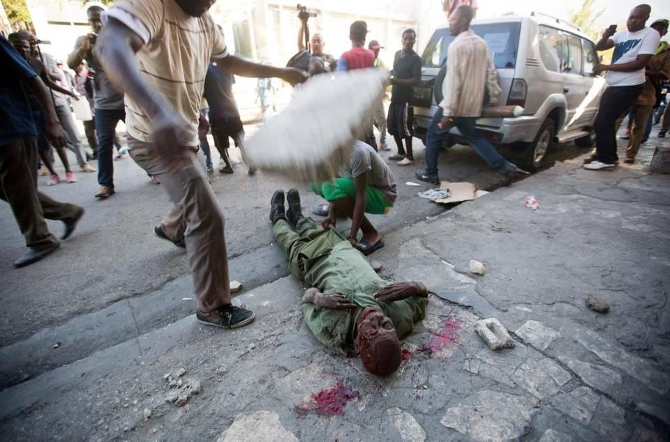 An anti-government protester drops a large cinderblock on the head of Neroce R. Ciceron, a former captain in Haiti's disbanded army, as other protesters and members of the press stand behind while he’s beaten to death in Port-au-Prince, Haiti, Friday, Feb. 5, 2016. Members of Haiti's abolished military clashed with protesters who were demanding the resignation of Haiti's President Michel Martelly.