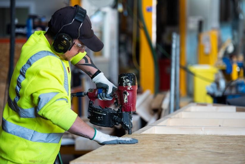 A person wearing a safety vest and gloves working on a piece of wood

Description automatically generated with low confidence